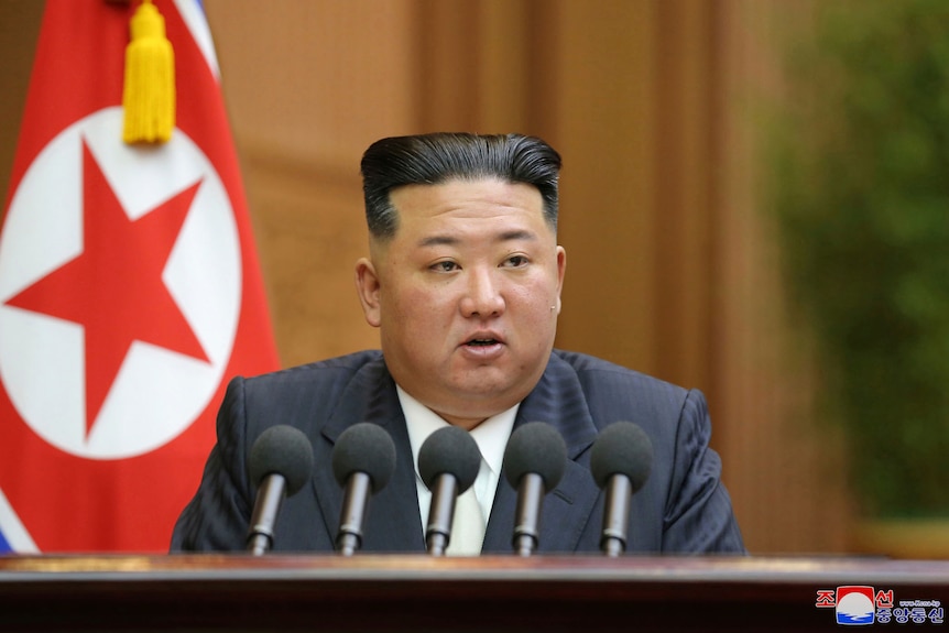 Il leader nordcoreano Kim Jong Un pronuncia un discorso seduto a una scrivania con un set di microfoni