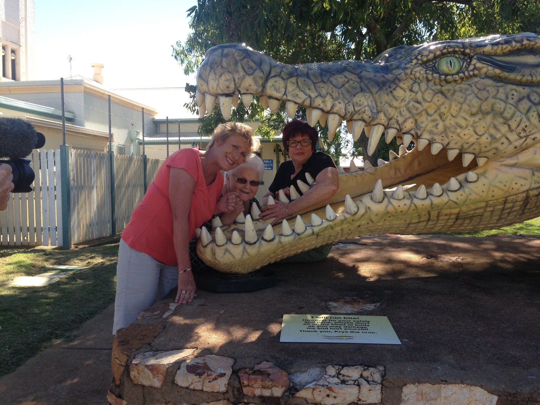 Three women smiling with their heads inside the mouth of an oversized crocodile statue.