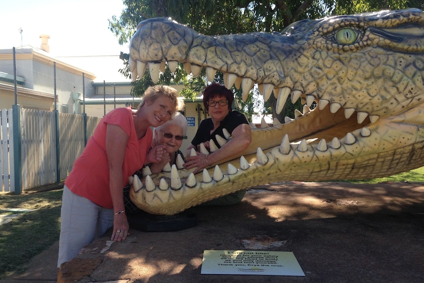 Three women smiling with their heads inside the mouth of an oversized crocodile statue.