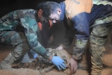 Two men carefully collect human bones from a dusty mass grave.