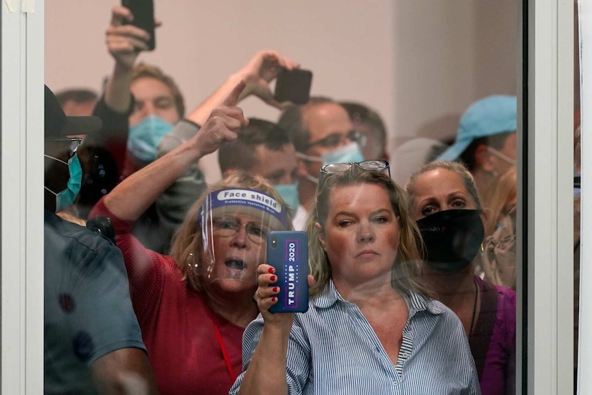 people stand outside a window holding up phones