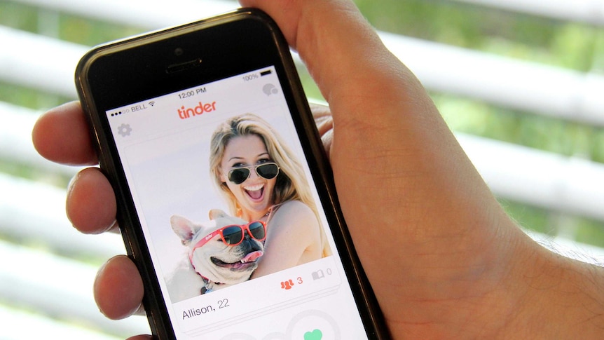 Hand holding a mobile phone showing the Tinder app.