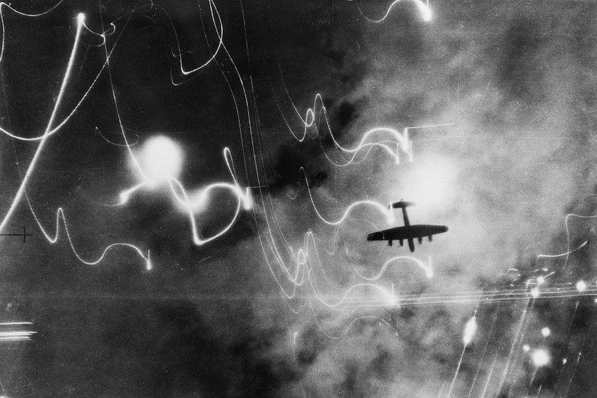 The silhouette of large aircraft in a night sky surrounded by lights leaving leaving trail patterns.