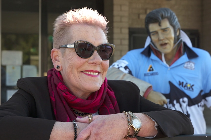 A woman in sunglasses poses in front of a statue of Elvis