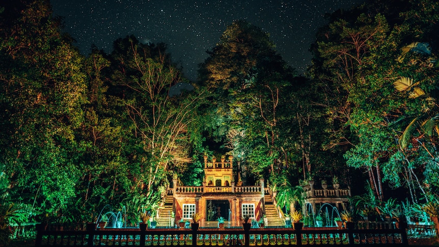 A photo of a castle at night in a forest, with everything all lit up by lights.