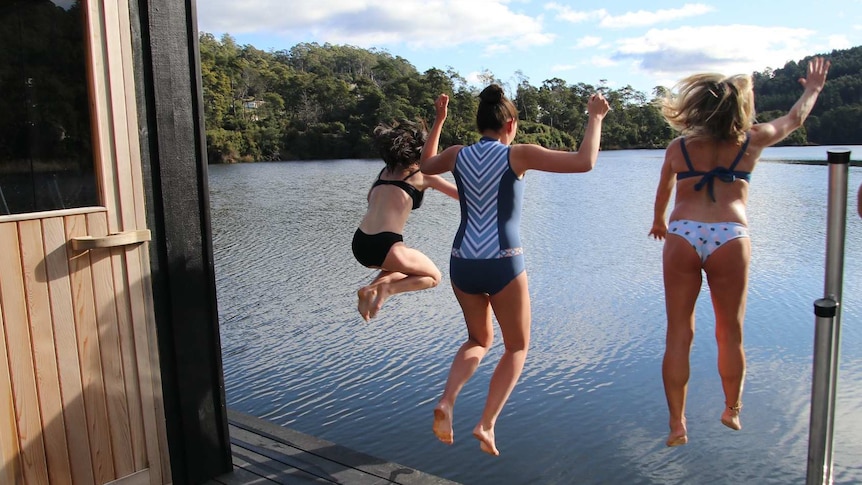 Three young women about to jump into a lake.