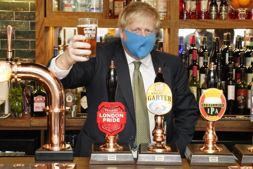 Boris Johnson, wearing a facemask, holds a pint of beer up.