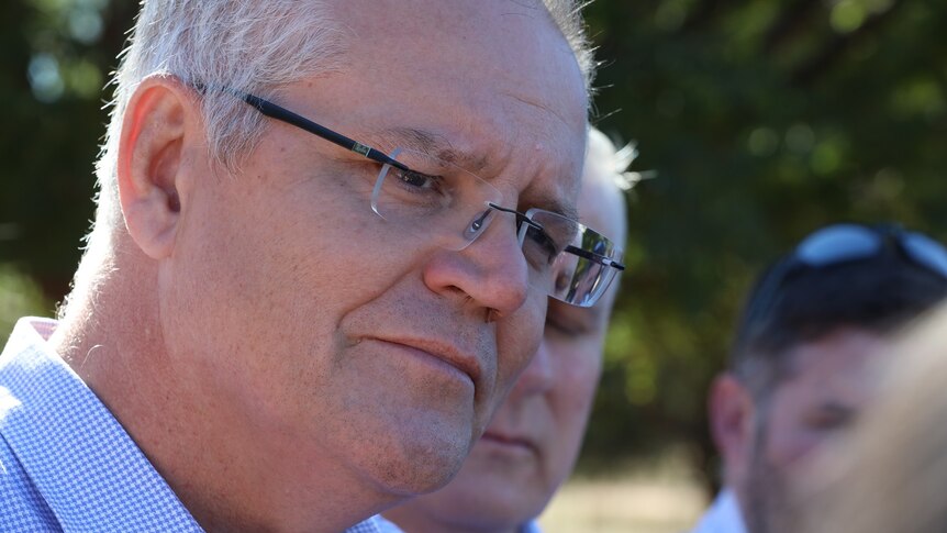 Close view of Scott Morrison with a serious expression on his face, standing outdoors on a sunny day.
