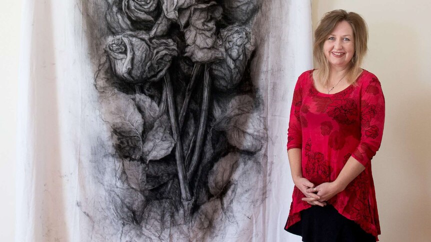 A woman stands next to a charcoal drawing of roses.