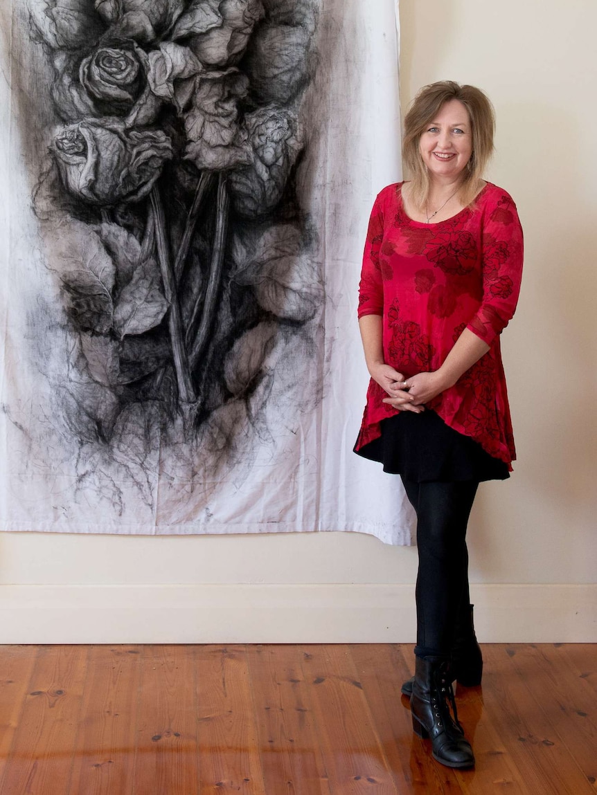 A woman stands next to a charcoal drawing of roses.