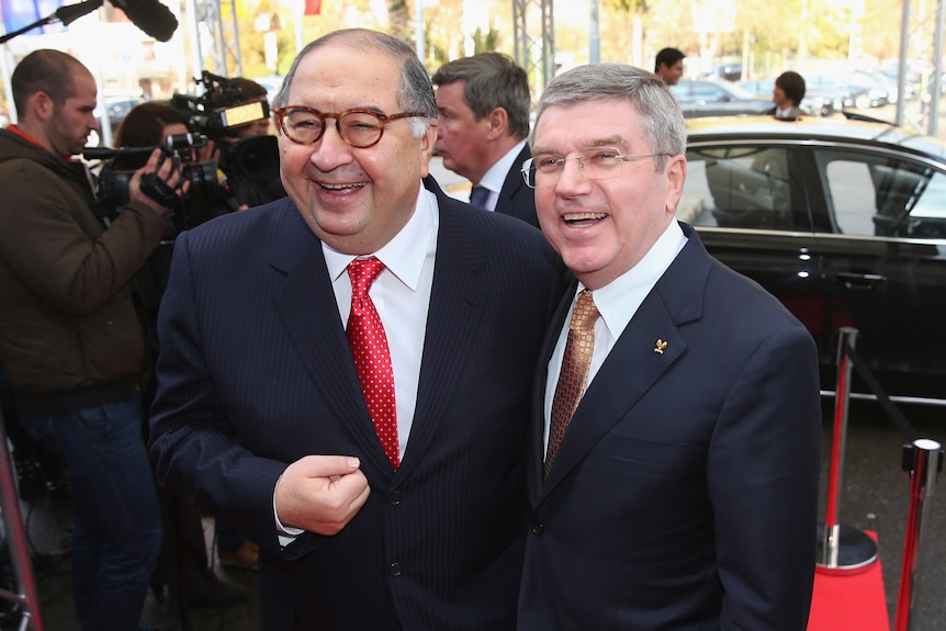 Two men in suits smile and laugh at the camera.