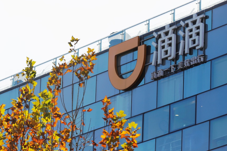 The Didi logo, an orange D on its side, is seen on a glass fronted building next to Chinese lettering.