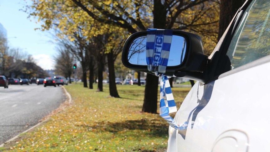 An abandoned car on a Canberra median strip with police tape on its mirror.
