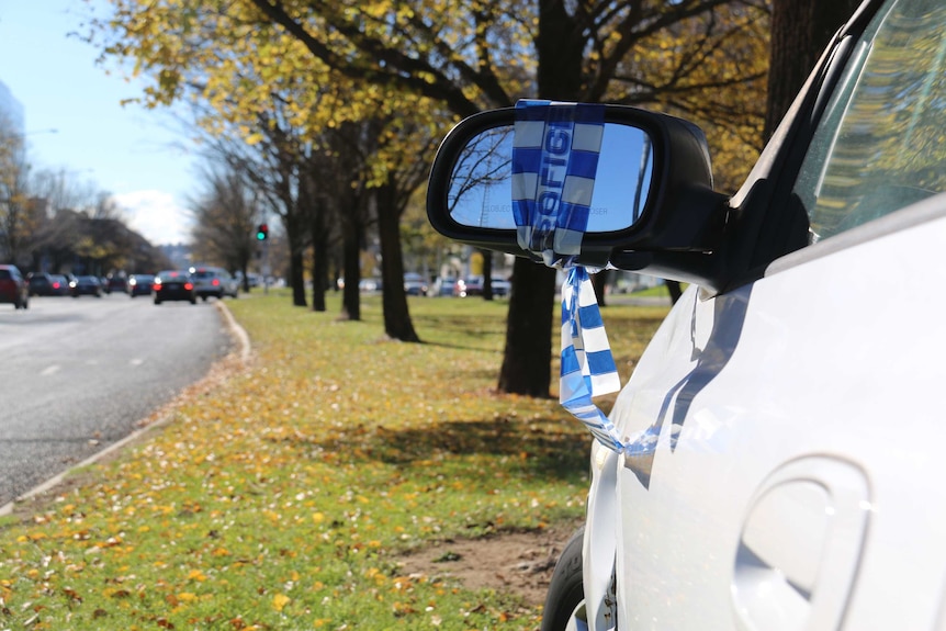 An abandoned car on a Canberra median strip with police tape on its mirror.