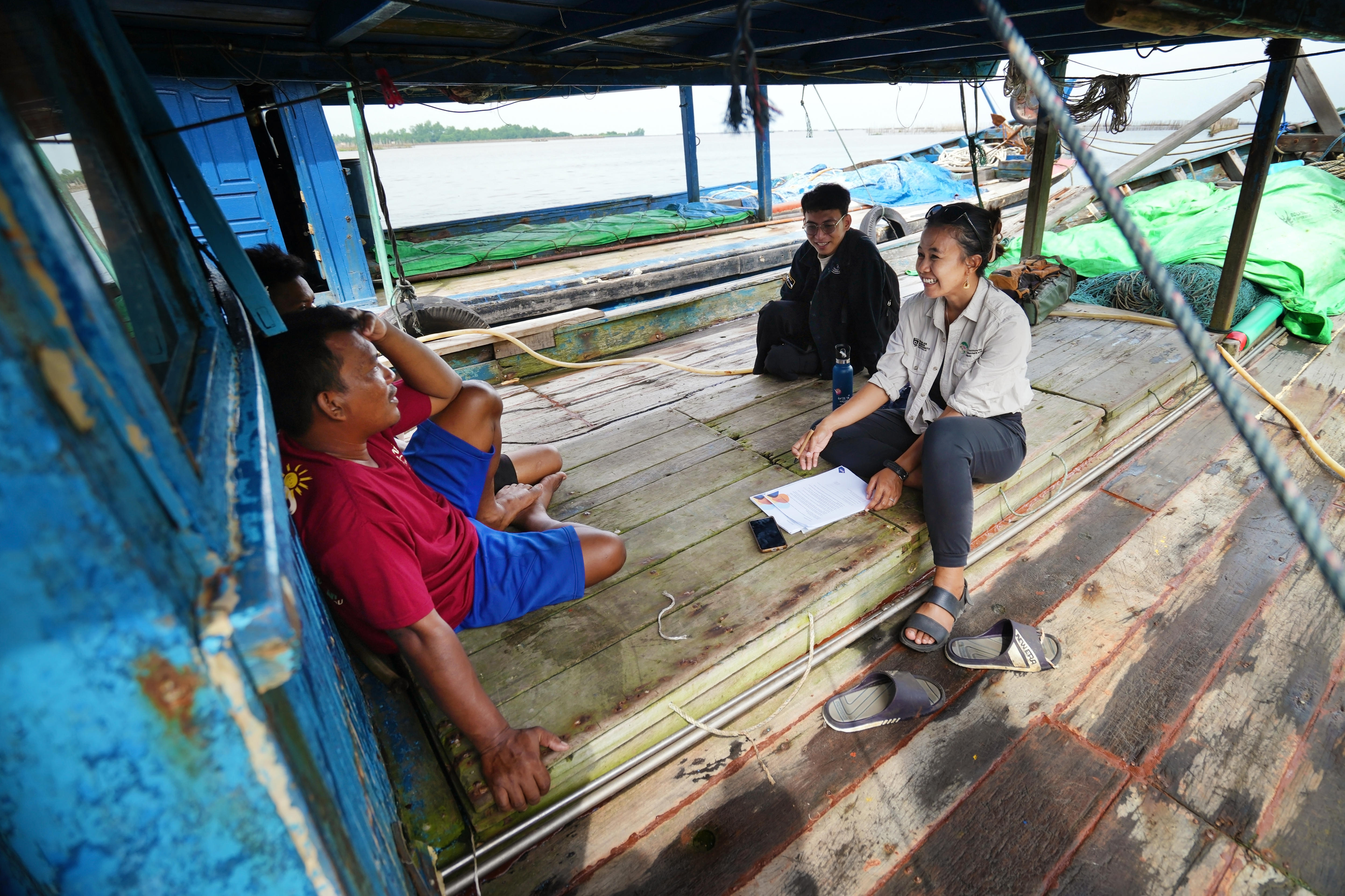 Una persona en un barco pesquero indonesio lleva una grabadora y una libreta mientras habla con un pescador.