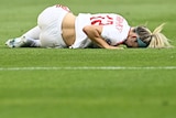 A female footballer player lies on the ground after injuring her knee.