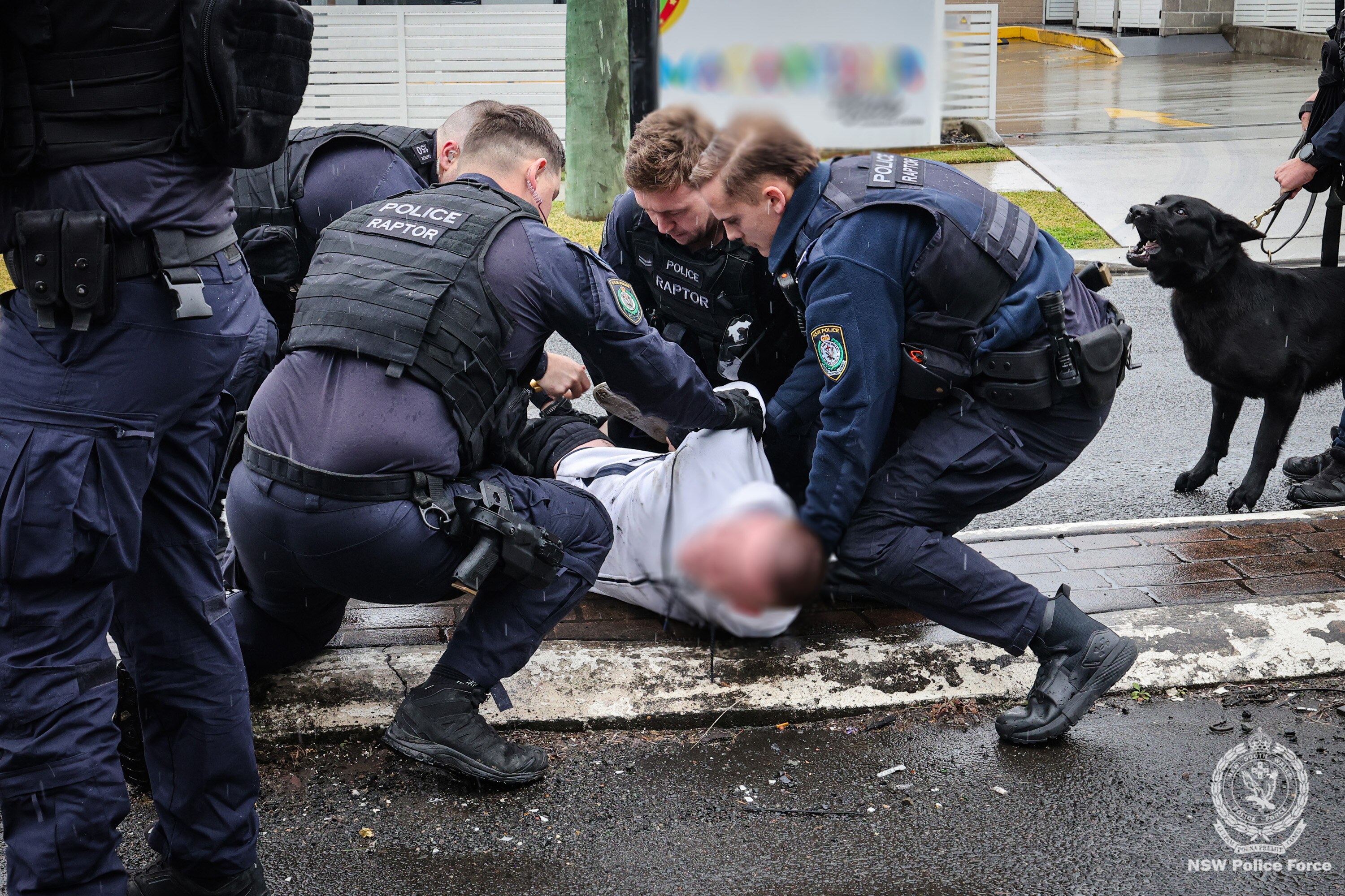 Unidentified NSW Police officers in navy uniform, with Raptor badge. Arrested man at centre with face blurred