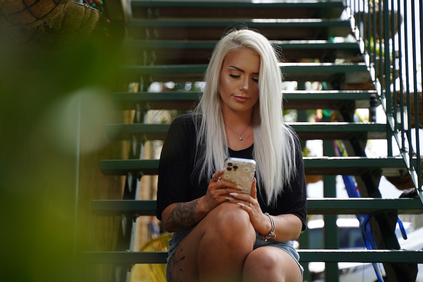 Kasharna Fyfe sits on an outdoor step and looks at her mobile phone
