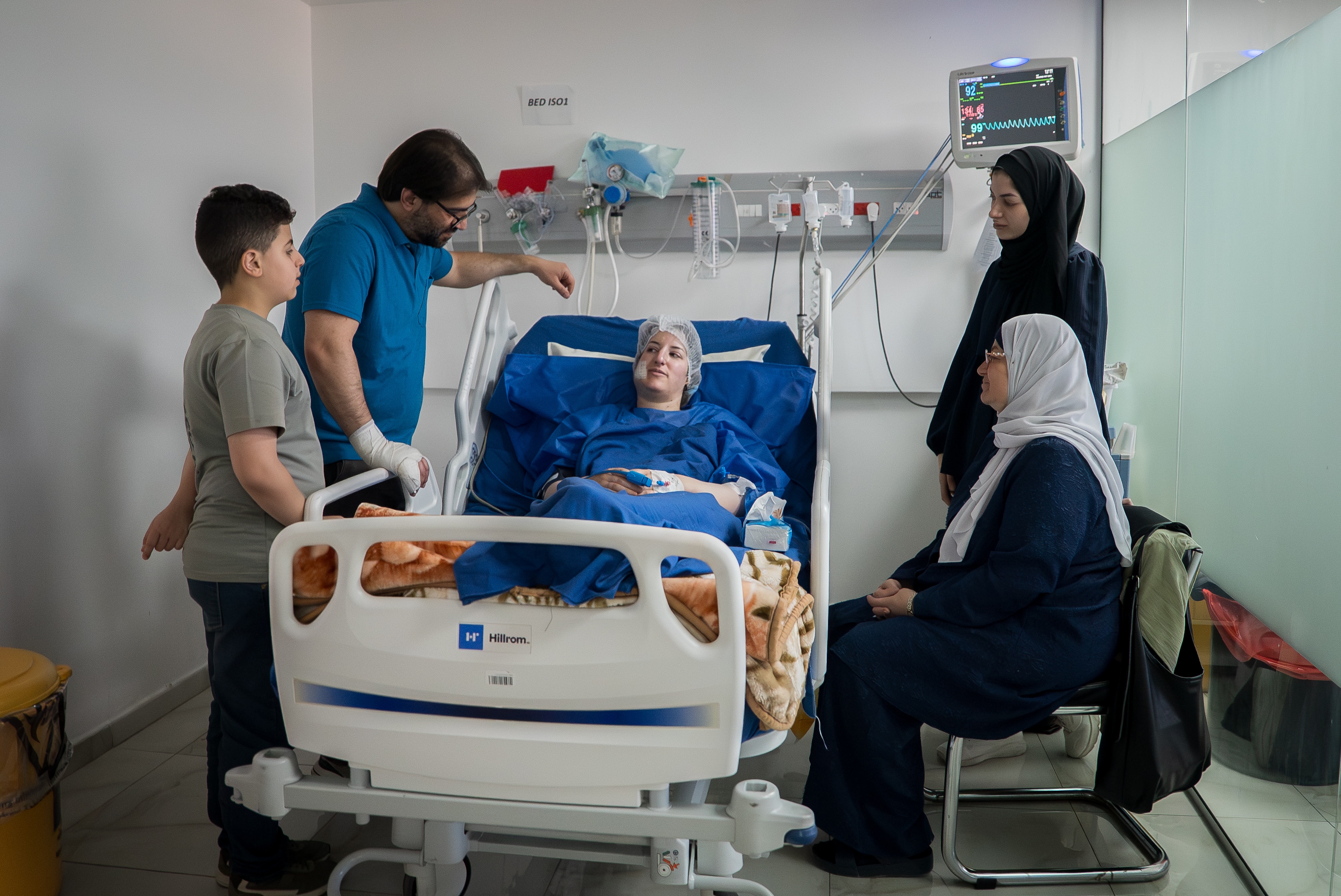 Dania Salameh lies in a hospital bed. Family members stand around her.