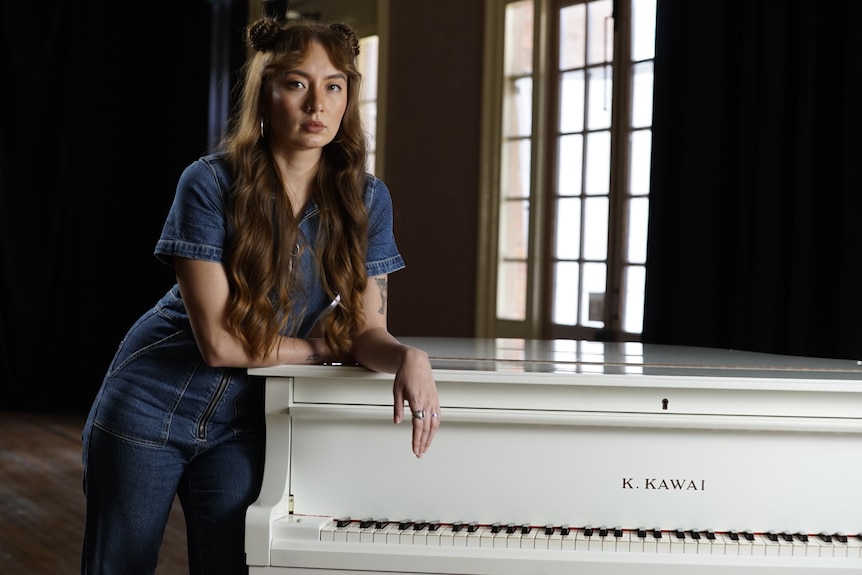 Deena Lynch leans against a piano.