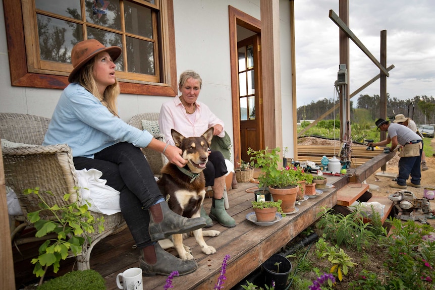 Srisa Heffernan and mother Amanda Heffernan-Buchan sit on chairs on their front porch. Srisa pats a dog.