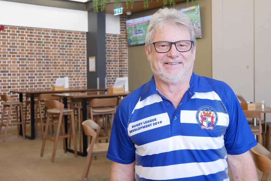 man with grey hair and beard and glasses stands in blue and white striped shirt