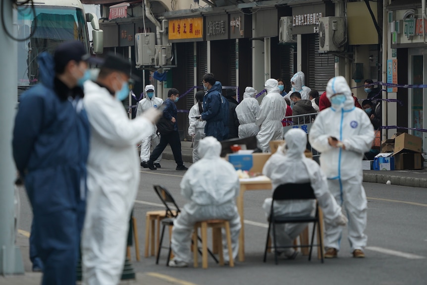 中国一栋公寓楼外，身着防护服的工人护送人们离开大楼