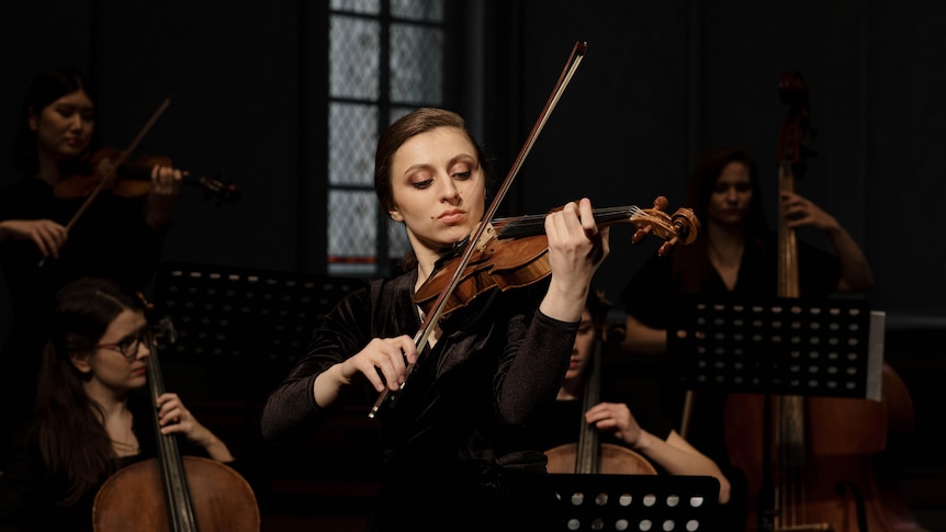 A woman playing violin in an orchestra