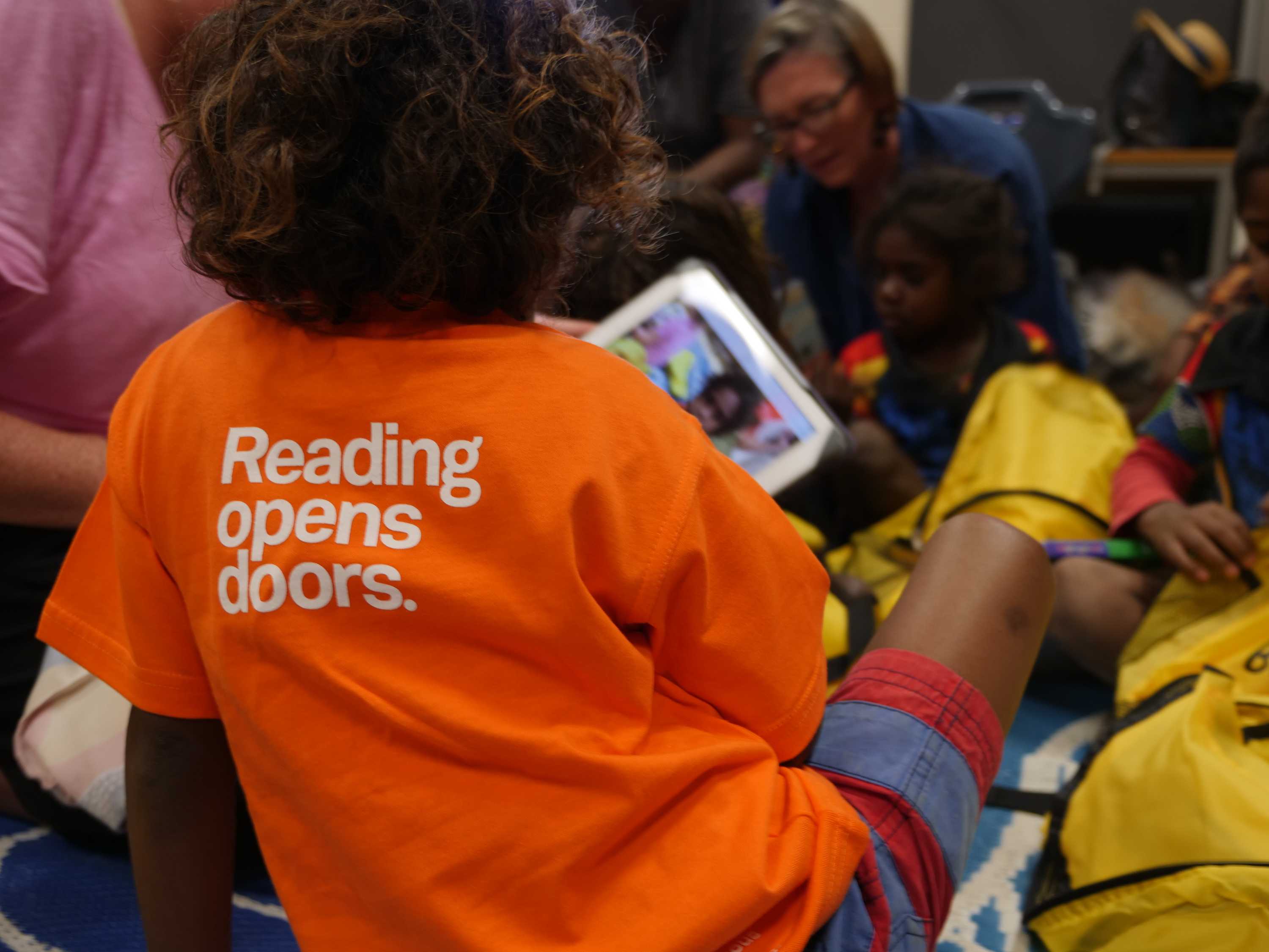 Aboriginal child wearing brightly coloured shirt reading 'Reading opens doors'.