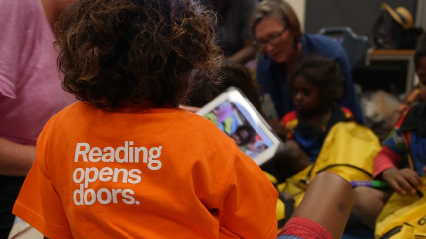 Aboriginal child wearing brightly coloured shirt reading 'Reading opens doors'.