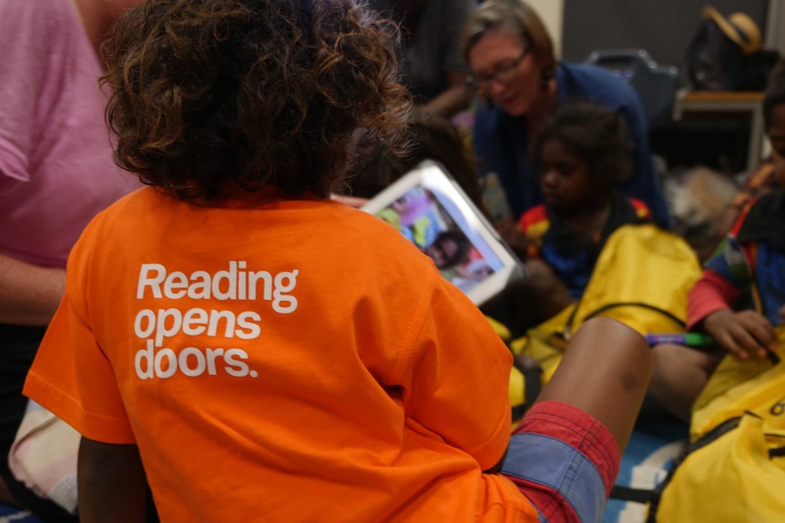 Aboriginal child wearing brightly coloured shirt reading 'Reading opens doors'.