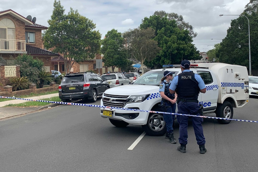Police stand behind police tape in a suburban street