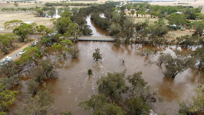 An aerial picture of an overflowing river in a rural area with a bridge just above the water level.