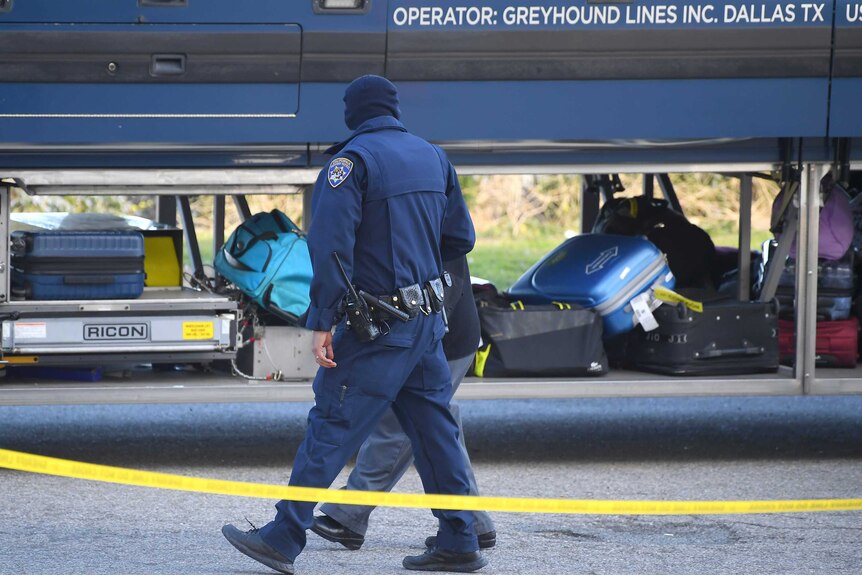 Investigators are seen outside of a Greyhound bus in front of the luggage compartment.