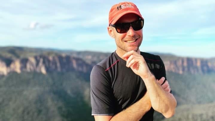 photo of a man in sunglasses on with a view of mountains behind him