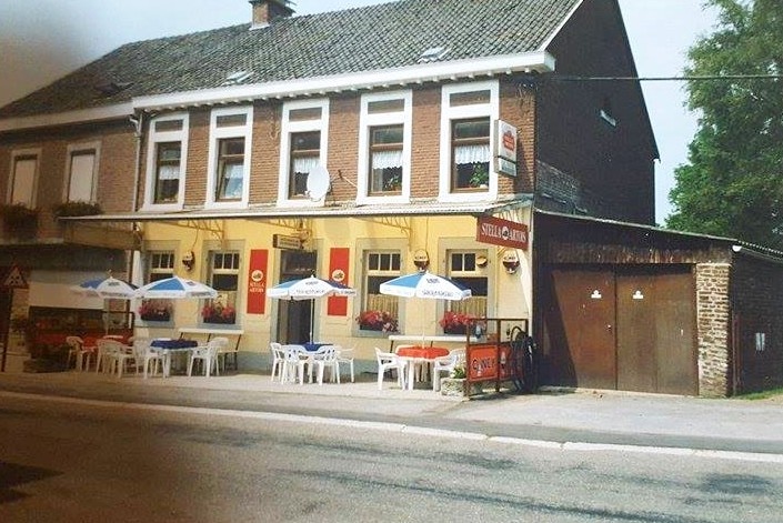 A sepia photograph from the 1990s of a two-storey brick beer house with plastic chair and umbrella shades outside.