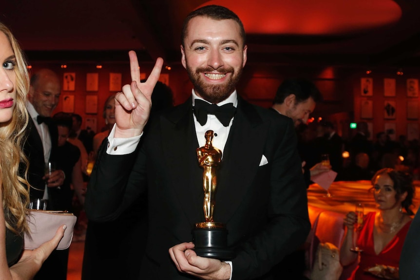Sam Smith signs peace while holding his Oscar.