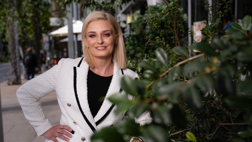 A woman in a white and black suit stands next to some leaves