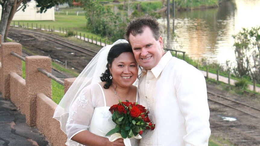 A photo of a bride and groom at their wedding in front of a lake and train tracks
