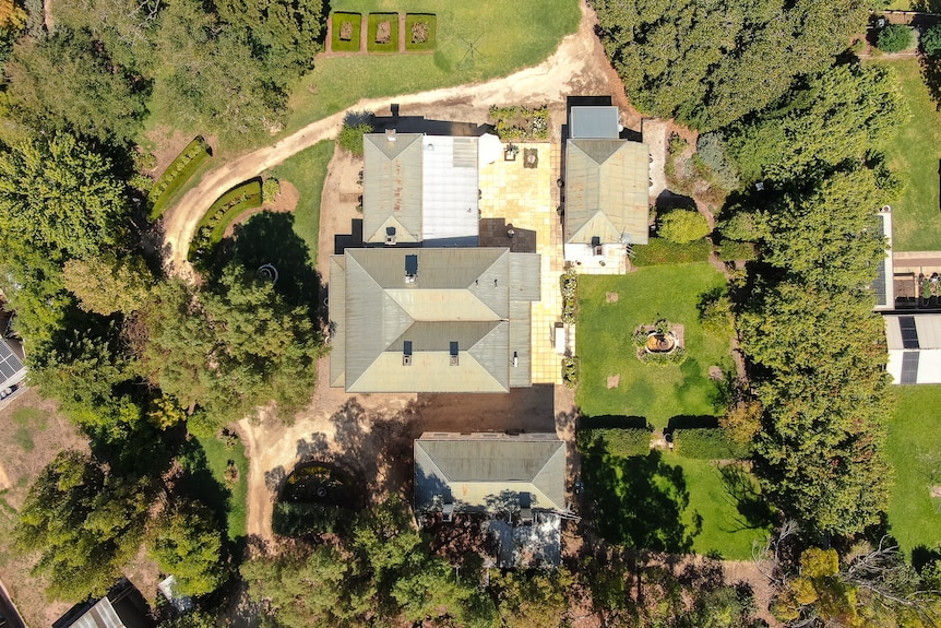 An aerial photo on a sunny day of three stone buildings surrounded by aesthetic landscaping and lawn.