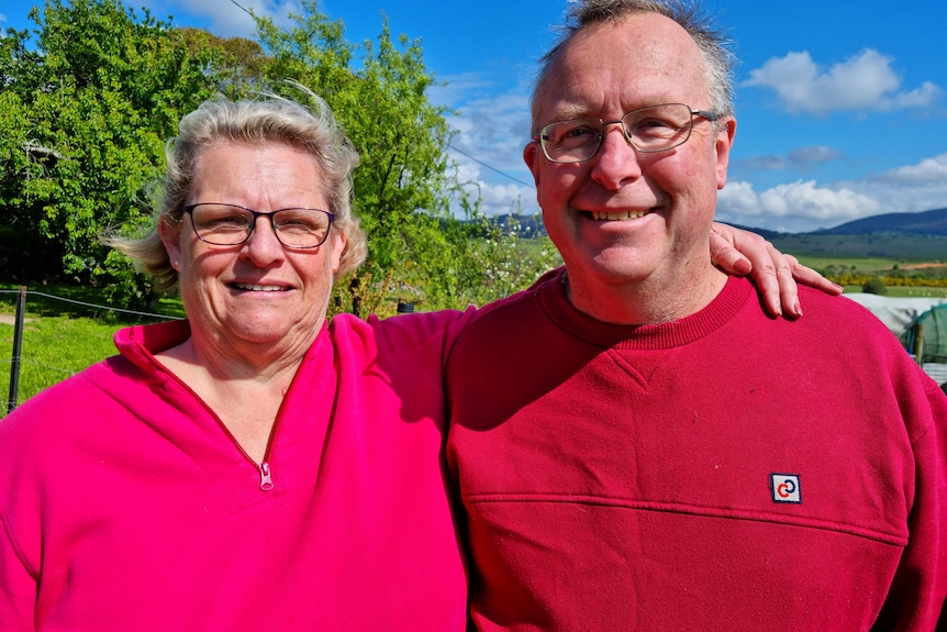 Brian and Elspeth Newby smile, standing outside wearing brightly colored t-shirts.