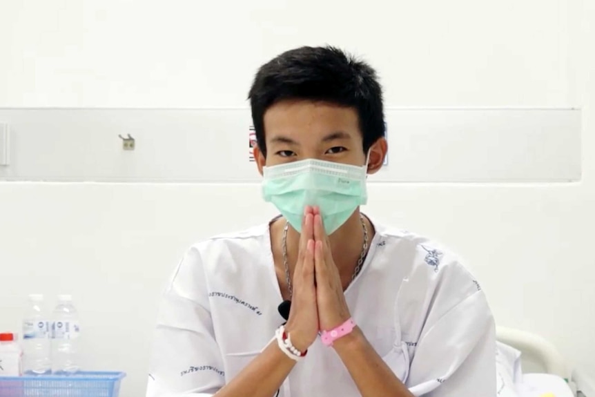 Boy wearing hospital gown and face mask holds hands together in prayer to say thankyou