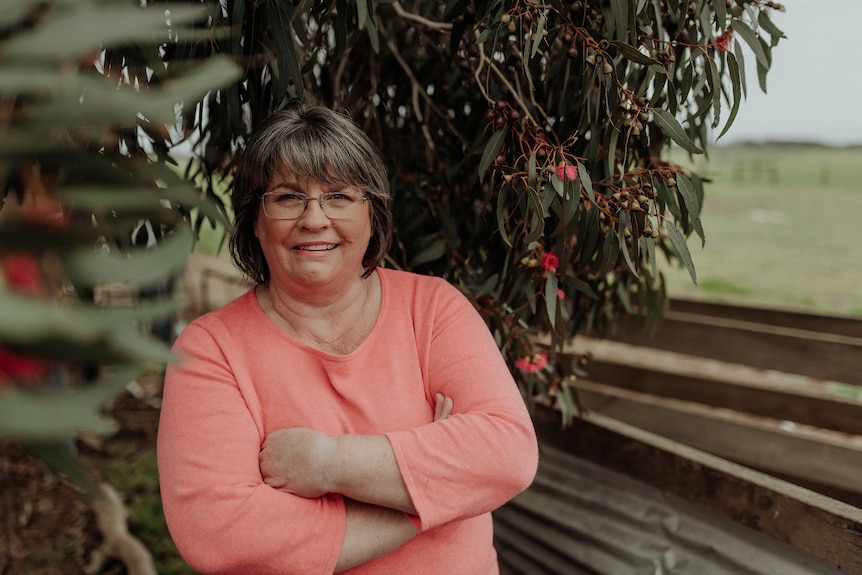 A woman stands smiling beneath a flowering gum.