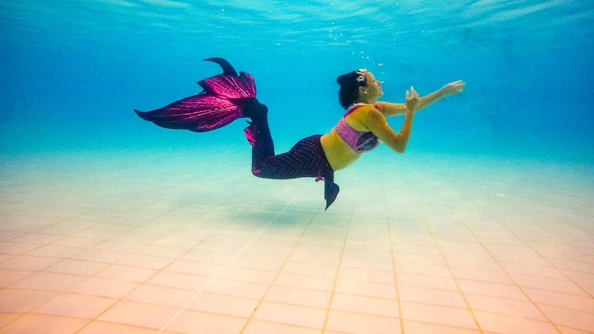 A woman in a mermaid tail swimming underwater in a pool.