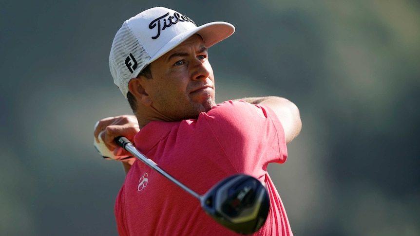 Adam Scott holds a pose with his golf club behind his back after playing a drive, wearing a pink shirt