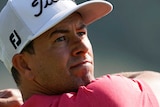 Adam Scott holds a pose with his golf club behind his back after playing a drive, wearing a pink shirt