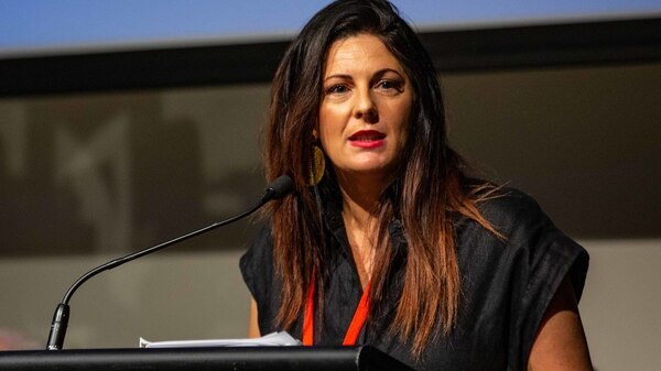 A woman with long dark hair speaks at a lectern