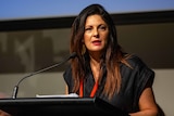A woman with long dark hair speaks at a lectern