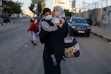 A woman in a headscarf walks holding a little boy in a face mask