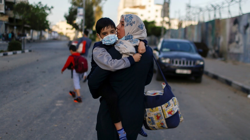 A woman in a headscarf walks holding a little boy in a face mask